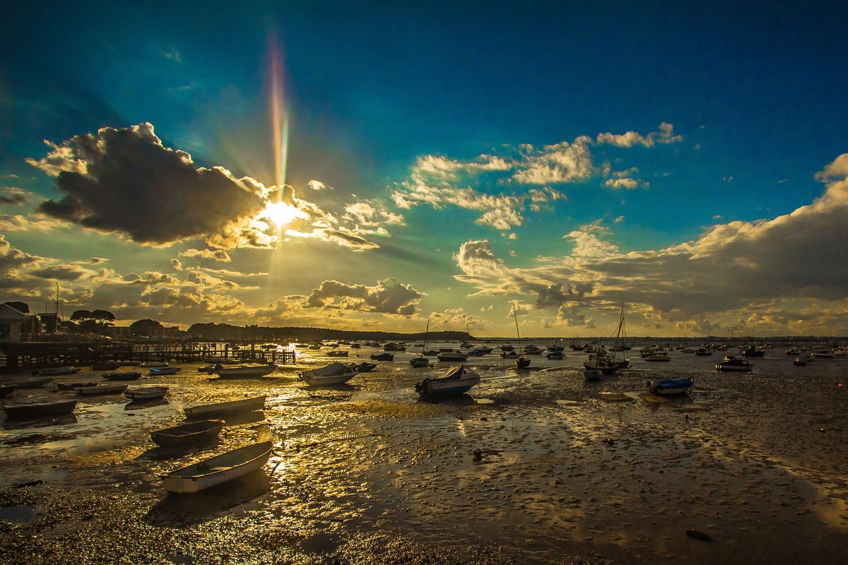 Small boats resting on wet harbour mud at low tide under a dramatic golden sunset sky