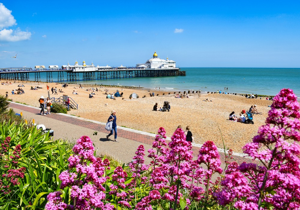 Victorian pier and pebble beach with people on the promenade and calm blue sea